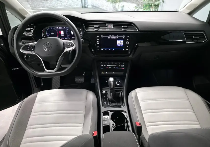 Vue intérieure avant du Volkswagen Touran 2024, tableau de bord noir avec sièges gris clair et console centrale équipée.