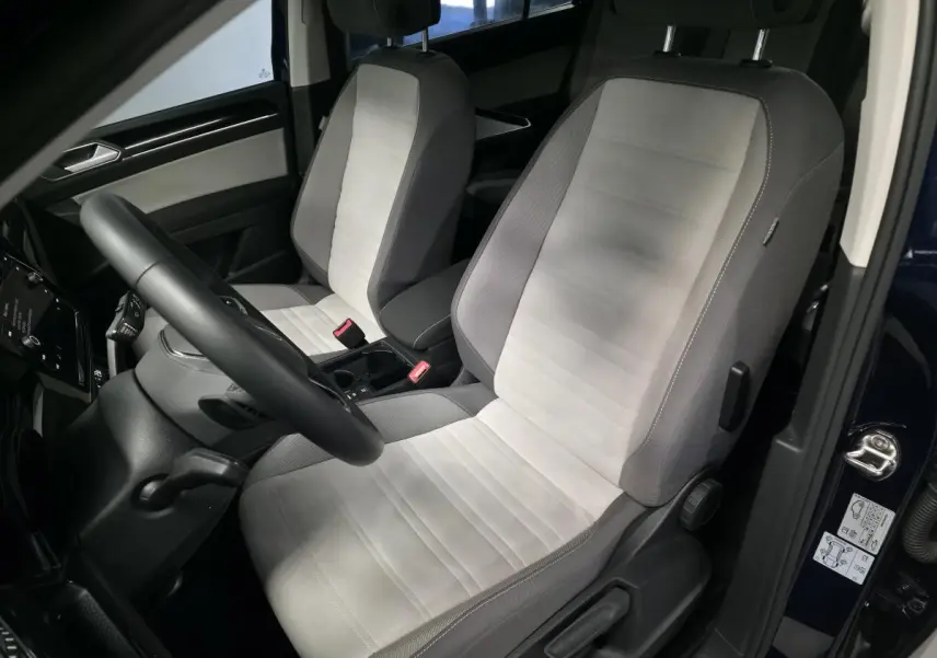 Intérieur côté conducteur du Volkswagen Touran bleu 2024, sièges en tissu gris clair et volant multifonction noir.