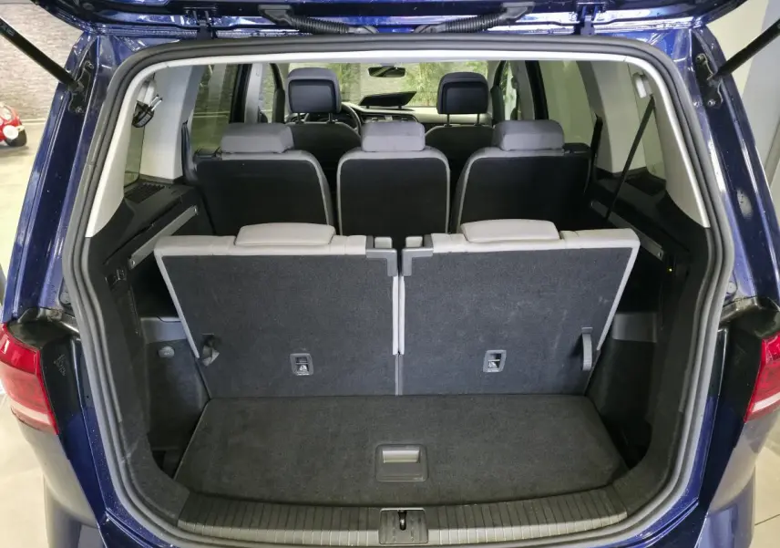 Vue arrière du coffre ouvert d'un Volkswagen Touran bleu 2024 montrant les sièges arrière rabattus et l'intérieur spacieux.