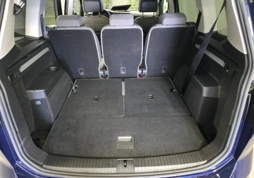 Coffre ouvert du Volkswagen Touran bleu 2024, vue arrière montrant les sièges arrière relevés et plancher de coffre plat.