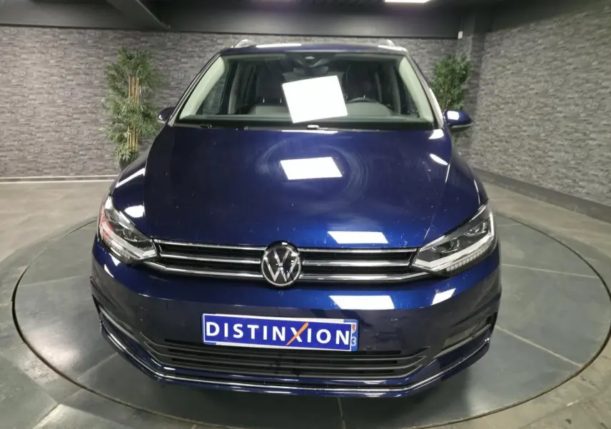 Vue frontale d'un Volkswagen Touran bleu métallisé 2024 avec calandre chromée et plaque Distinxion.
