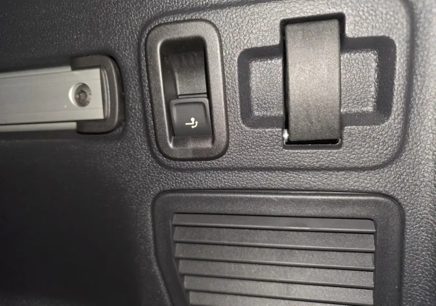 Gros plan sur le bouton de rabattement électrique des sièges dans le coffre du Volkswagen Touran bleu 2024.