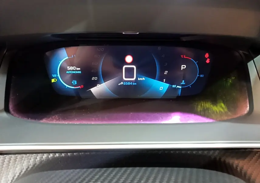 Affichage numérique du tableau de bord de la Peugeot 208 gris foncé, montrant vitesse, autonomie et indicateurs.