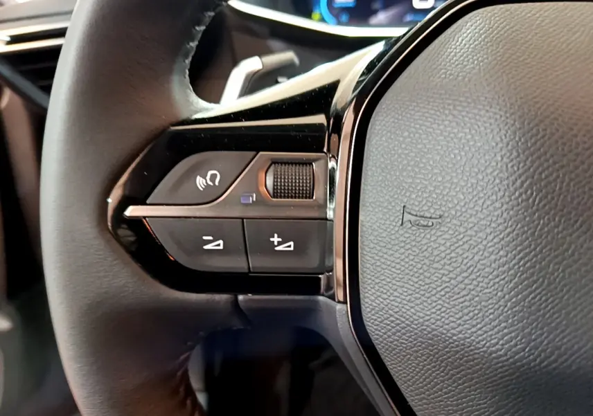 Gros plan sur la partie gauche du volant cuir du Peugeot 208 gris foncé, avec commandes audio intégrées.