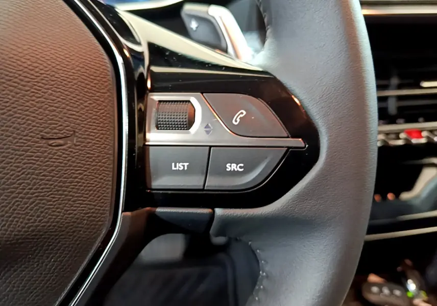 Gros plan sur les commandes gauche du volant cuir noir de la Peugeot 208 gris foncé, avec boutons LIST et SRC visibles.