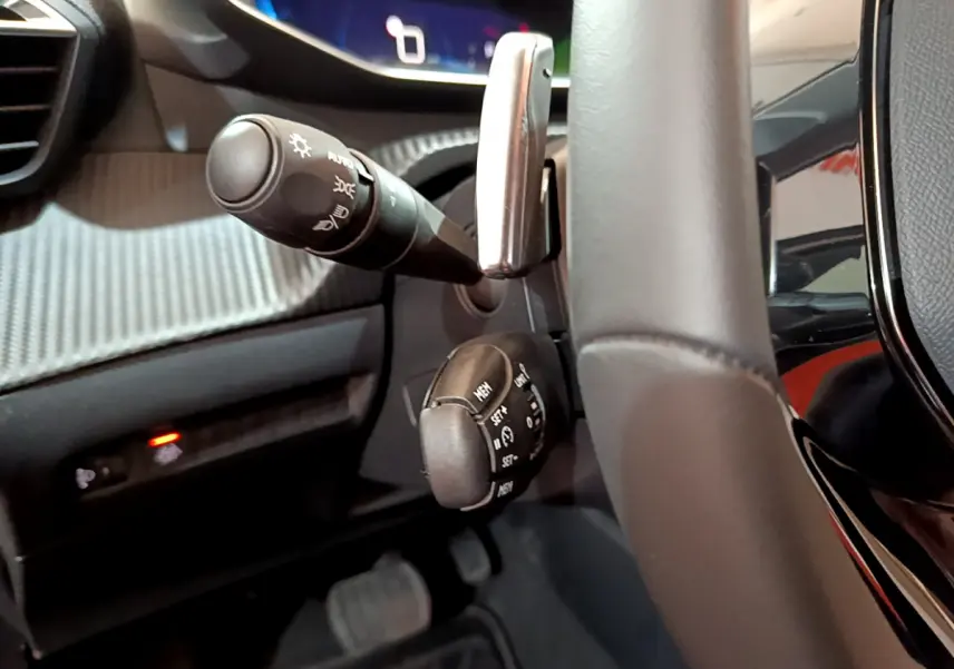 Gros plan sur les commandes au volant cuir de la Peugeot 208 gris foncé, avec tableau de bord numérique en arrière-plan.