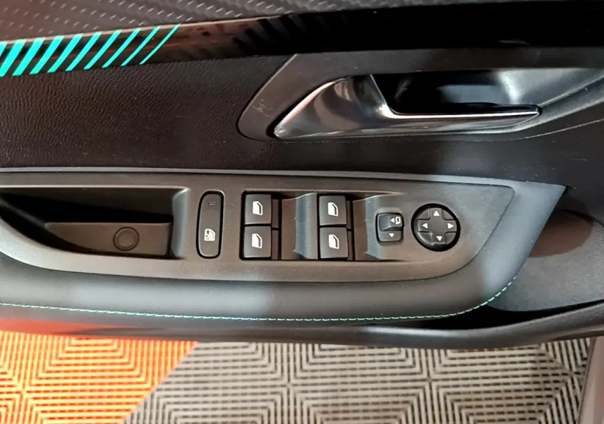 Commande des vitres et rétroviseurs sur la porte côté conducteur d'une Peugeot 208 gris foncé avec surpiqûres bleues.