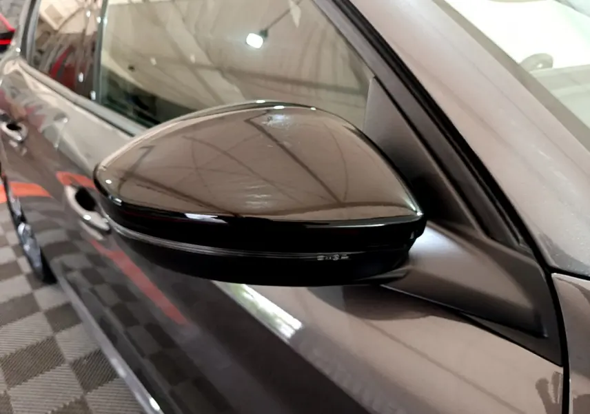 Rétroviseur côté gauche noir brillant d’une Peugeot 208 gris foncé vue en gros plan intérieur garage.