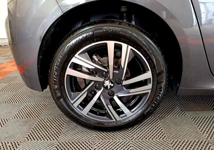 Gros plan sur la roue avant gauche gris foncé d'une Peugeot 208 avec jante alliage et logo lion central.