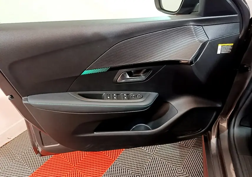 Vue intérieure côté gauche de la porte avant d'une Peugeot 208 gris foncé avec insert décoratif carbone et commandes électriques.