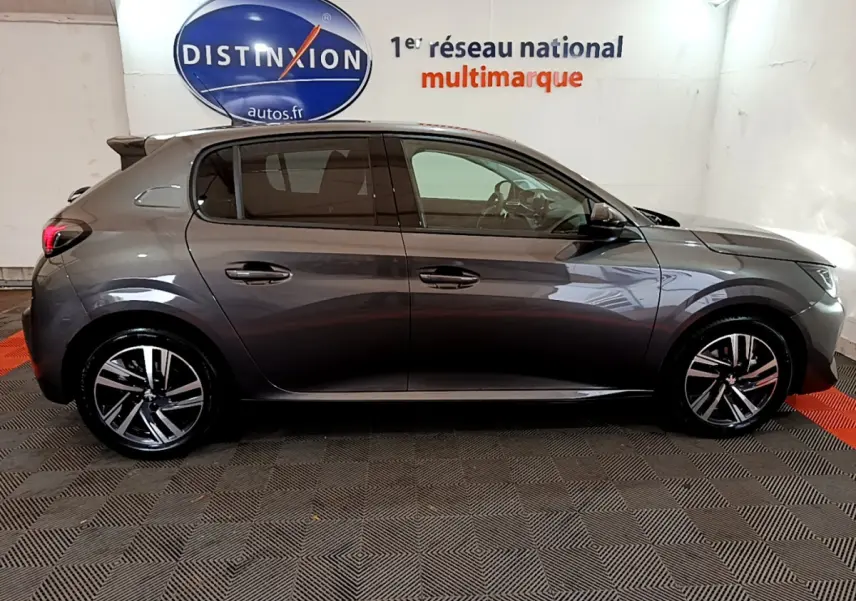 Profil côté droit d'une Peugeot 208 gris foncé 2022 avec jantes alliage et vitres teintées, en intérieur showroom.