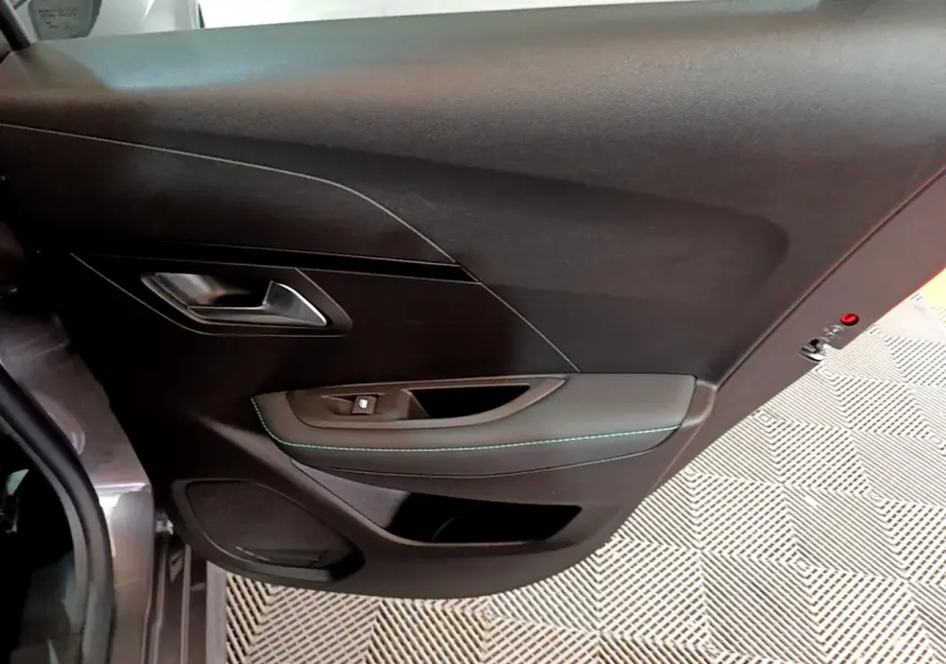 Vue intérieure du panneau de porte avant gauche de la Peugeot 208 gris foncé avec surpiqûres vertes et commande de vitre.