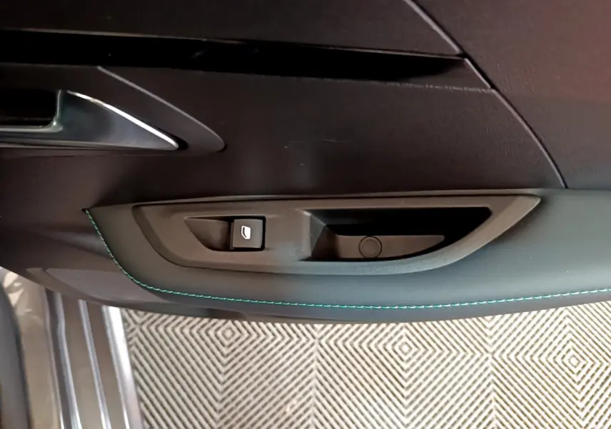 Poignée intérieure côté gauche de la porte d'une Peugeot 208 gris foncé avec couture bleue et bouton de verrouillage.