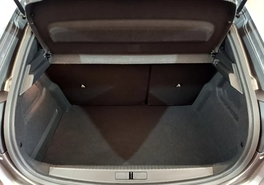 Coffre ouvert vu de l'arrière d'une Peugeot 208 gris foncé, montrant l'espace de chargement vide et les sièges rabattables.