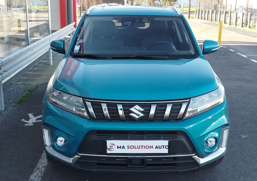 Vue frontale d'un Suzuki Vitara 2023 turquoise métallisé avec calandre chromée et antibrouillards ronds intégrés.