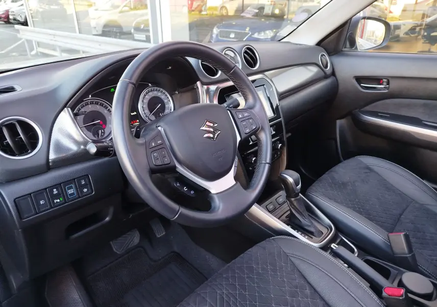 Vue intérieure côté conducteur du Suzuki Vitara 2023, volant cuir, tableau de bord noir et sièges tissu noir avec surpiqûres.