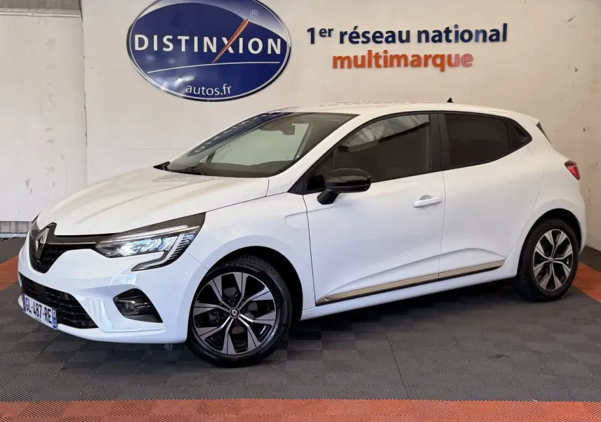 Renault Clio Business blanc vue 3/4 avant droit, jantes noires et logo Distinxion en arrière-plan.