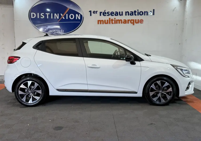 Profil droit d'une Renault Clio Business TCe 100 GPL blanche, avec jantes alliage et rétroviseurs noirs, en intérieur showroom.