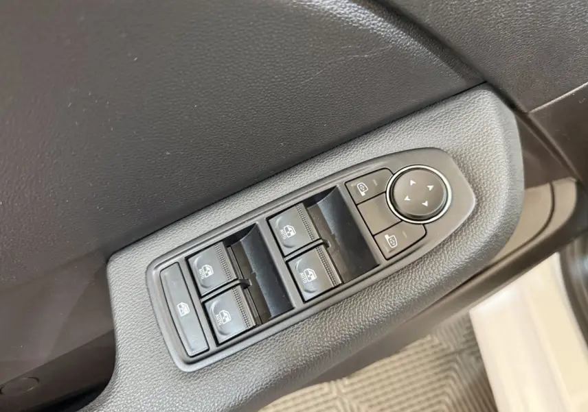 Gros plan sur les commandes des vitres électriques et rétroviseurs sur la porte côté gauche d'une Renault Clio blanche.