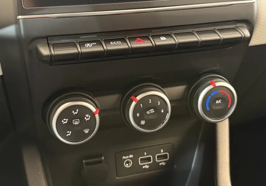 Gros plan sur les commandes de climatisation et les ports USB du tableau de bord noir de la Renault Clio blanche.