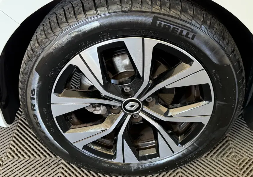 Gros plan sur la roue avant droite d'une Renault Clio blanche avec jante alliage bicolore et pneu Pirelli.