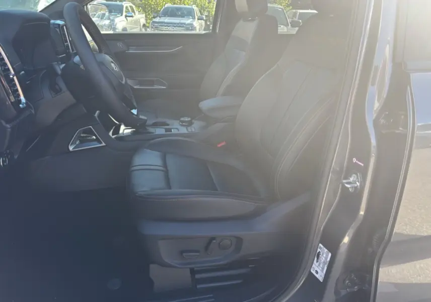Vue intérieure côté conducteur du Ford Ranger gris carbone 2025, sièges cuir noirs avec surpiqûres orange et logo Wildtrak brodé.