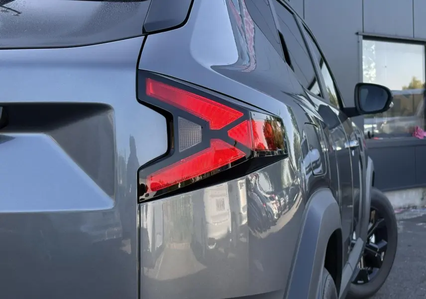 Vue arrière côté droit du Dacia Duster 2026 gris schiste, mettant en valeur le feu arrière en forme de X et les jantes noires.