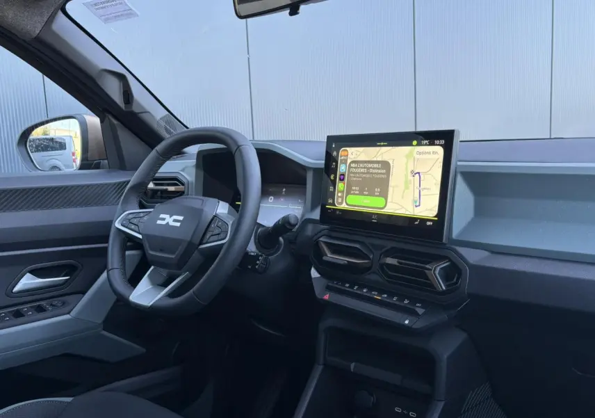 Vue intérieure côté conducteur du Dacia Duster 2026 gris, avec écran tactile central et volant multifonctions.