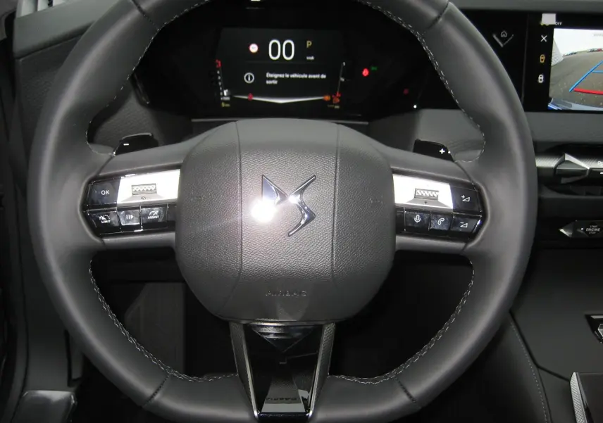 Gros plan sur le volant en cuir noir du DS4 2024 avec commandes intégrées et tableau de bord numérique en arrière-plan.