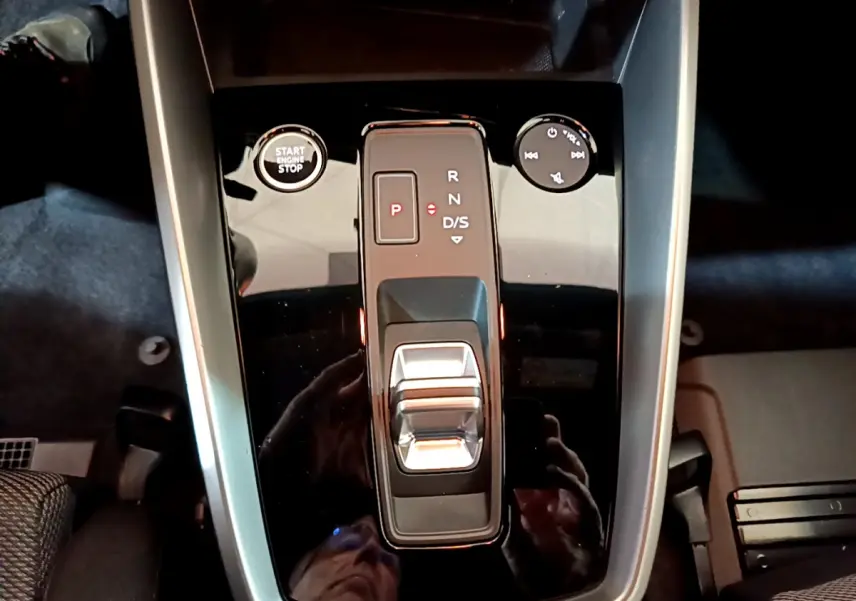 Vue plongeante sur la console centrale noire brillante de l'Audi A3 35 TFSI avec levier de vitesses automatique et bouton start-stop.