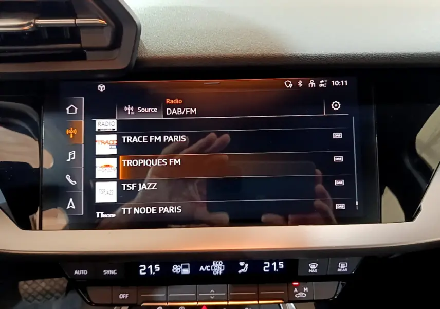 Écran tactile central de l'Audi A3 35 TFSI bleu, affichant les stations radio DAB/FM en intérieur.