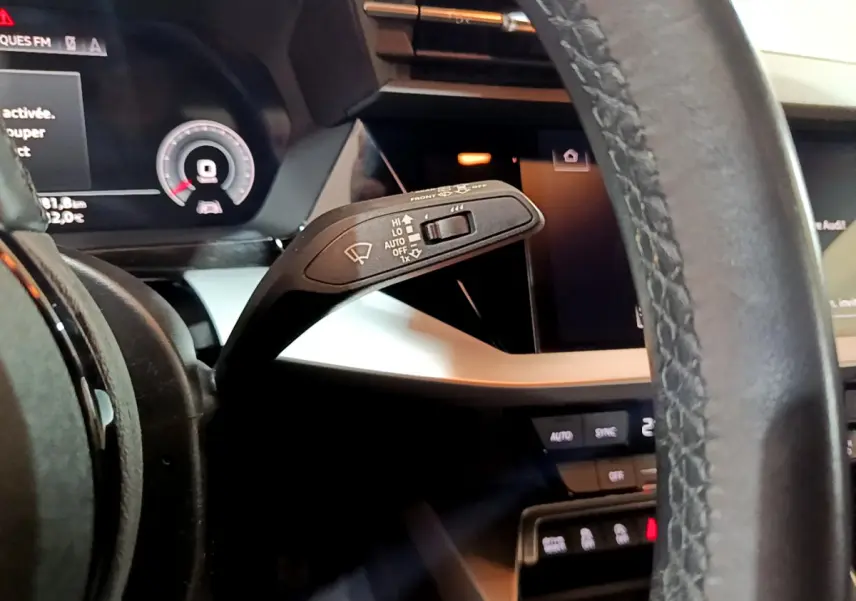 Gros plan sur le commodo d’essuie-glace à gauche du volant cuir dans l’habitacle de l’Audi A3 bleu 2023.