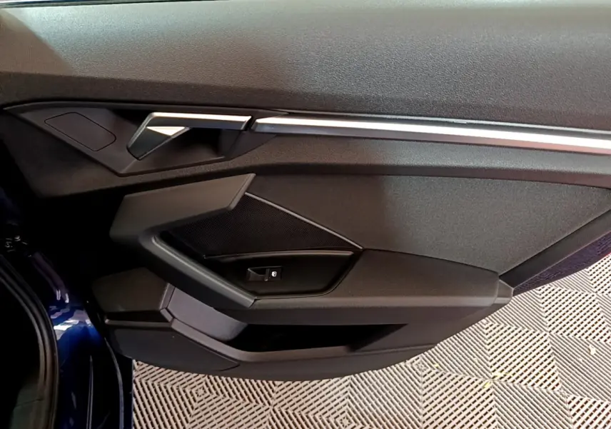 Vue rapprochée de la porte côté gauche de l'Audi A3 bleu 2023, avec poignée et commandes intégrées.
