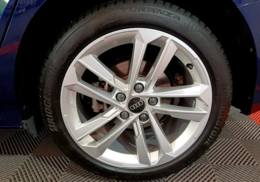 Gros plan sur la jante alliage argentée avec logo Audi d'une A3 bleu 35 TFSI 150 MHEV S Tronic Business Line 2023