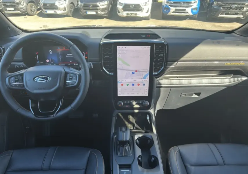 Vue intérieure frontale du Ford Ranger Wildtrak 2025 avec tableau de bord noir, écran tactile vertical et volant cuir multifonctions.