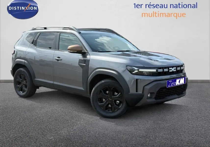 Dacia Duster gris 3/4 avant droit avec jantes noires et rétroviseurs couleur bronze sur fond clair.