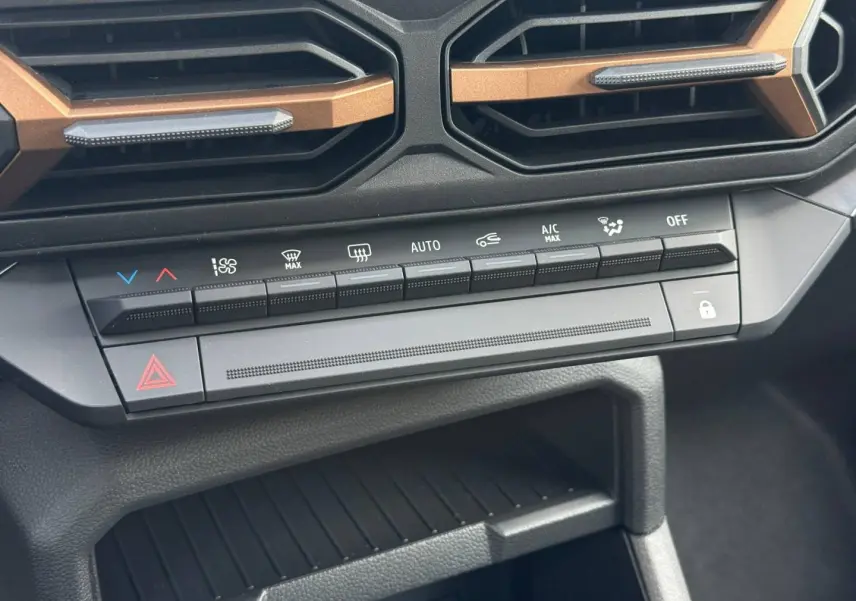 Détail du tableau de bord du Dacia Duster 2026 montrant les commandes de climatisation et les aérateurs avec inserts bronze.