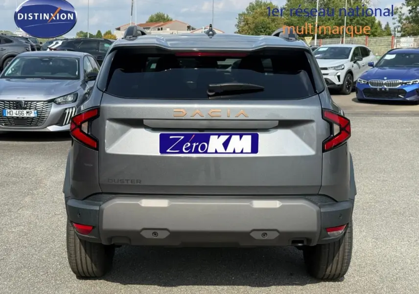 Vue arrière d'un Dacia Duster gris 2026 avec feux arrière en forme de C et logo DACIA en lettres dorées.
