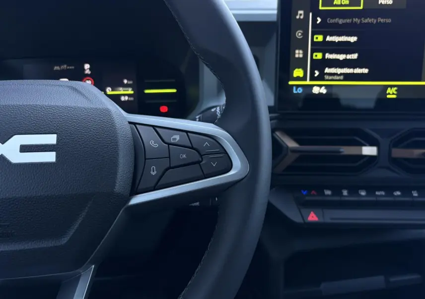 Gros plan sur le volant à droite et l’écran tactile central du tableau de bord du Dacia Duster blanc Glacier 2026.