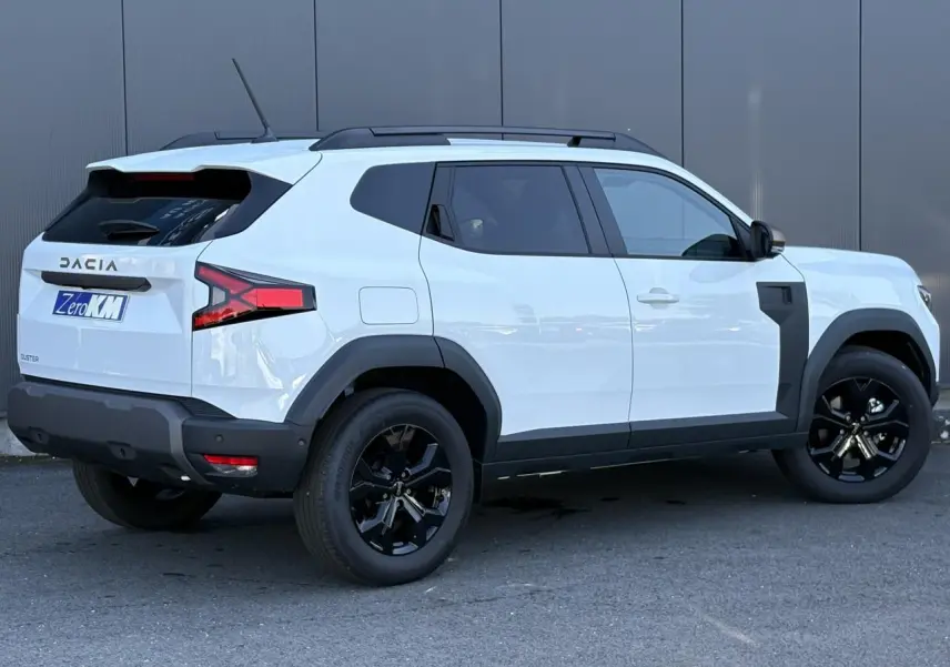 Vue 3/4 arrière droite du Dacia Duster 2026 blanc Glacier avec jantes noires et barres de toit noires.
