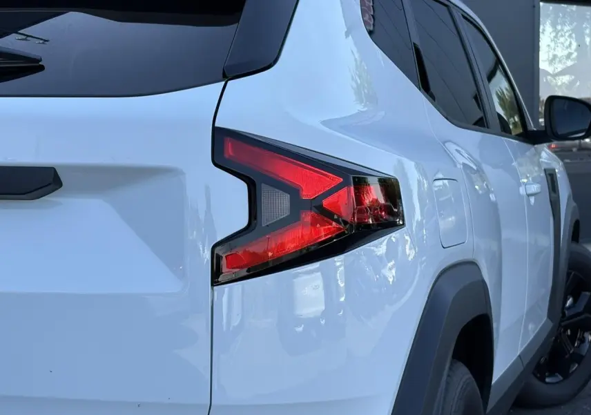 Vue arrière côté gauche du Dacia Duster blanc Glacier 2026 avec feux arrière en forme de flèche et vitres surteintées.