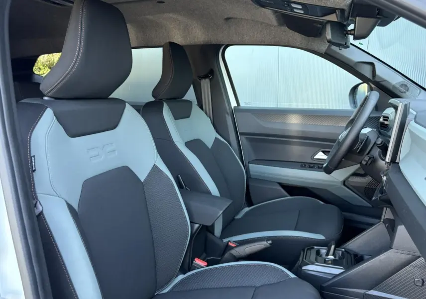 Vue intérieure côté conducteur du Dacia Duster 2026, sièges bicolores noir et gris avec accoudoir central.