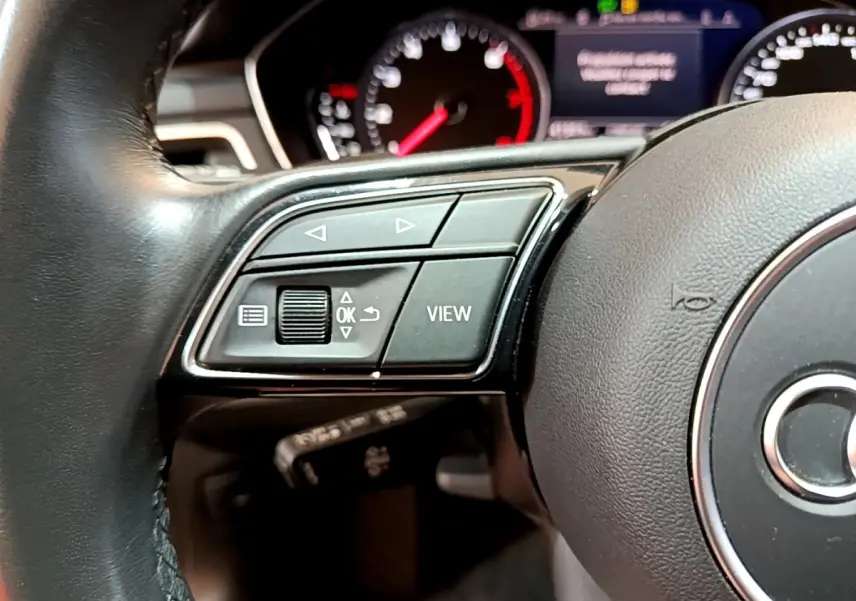 Gros plan sur le volant cuir noir de l'Audi A5 2021, côté gauche avec commandes multifonctions et tableau de bord en arrière-plan.