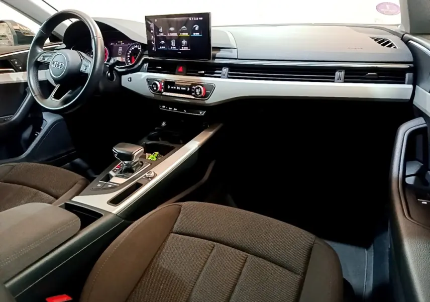 Intérieur Audi A5 2021 vu côté conducteur, tableau de bord noir avec écran central tactile et sièges tissu marron.