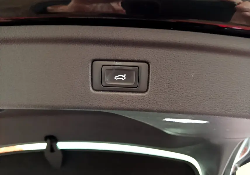 Bouton d'ouverture électrique du coffre vu en gros plan à l'intérieur du hayon d'une Audi A5 noire 2021.