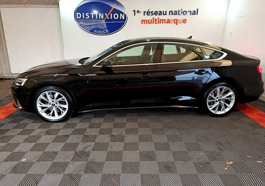 Profil côté gauche d'une Audi A5 noire 2021 stationnée en intérieur avec jantes argentées et toit panoramique.