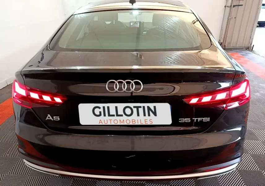 Vue arrière d'une Audi A5 noire 35 TFSI avec feux LED allumés et logo Audi bien visible.