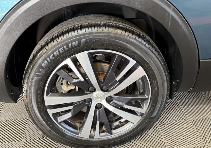 Gros plan sur la roue avant droite d’un Peugeot 5008 bleu, avec jante alliage bicolore et pneu Michelin.