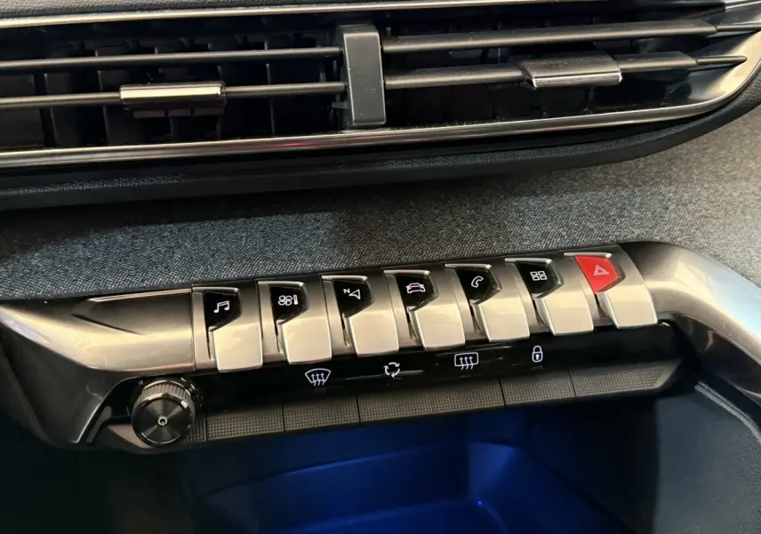 Gros plan sur la console centrale du Peugeot 5008 bleu, montrant les boutons de commande et la ventilation.