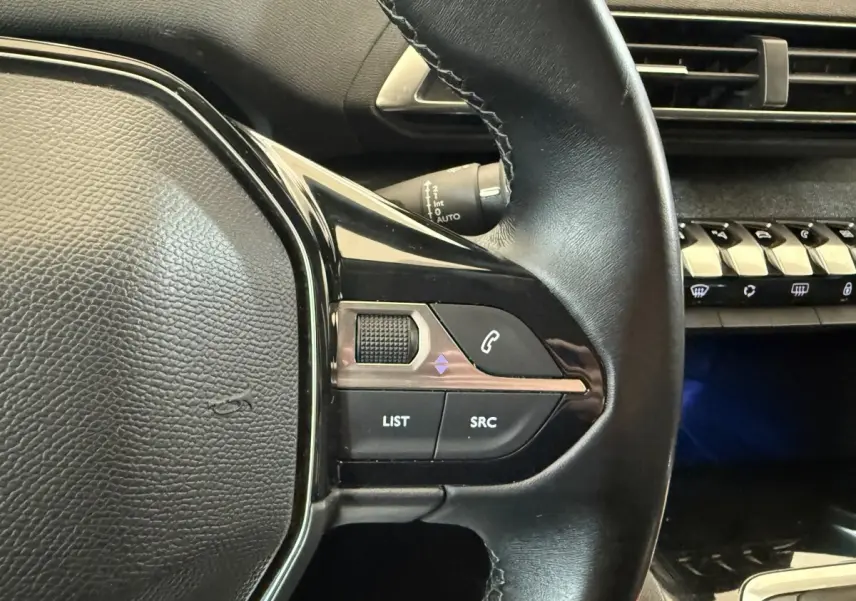 Gros plan sur le volant cuir multifonctions noir côté gauche du Peugeot 5008 bleu, avec commandes audio et téléphone.